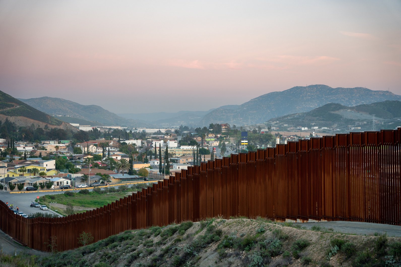 International Border Wall Between Tecate California and Tecate Mexico Near Tijuana Baja California Norte at Dusk Under Stunning Sunset with View of the City From the USA